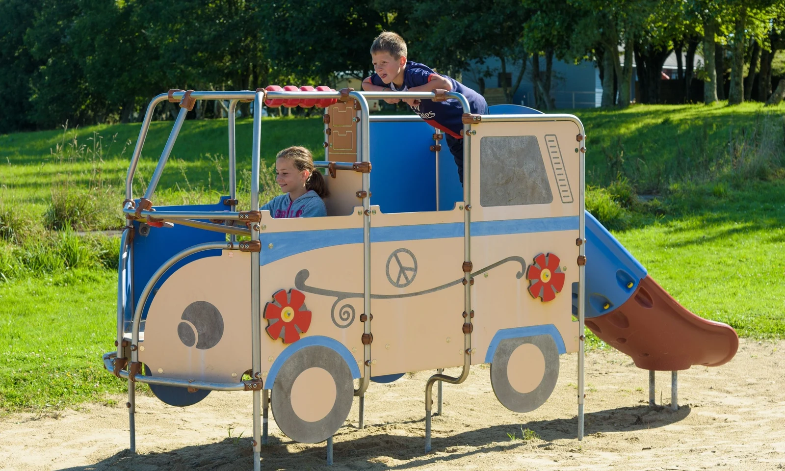 Playground bus structure with two children playing, situated on sandy ground near grassy area and trees at Domaine de Mesqueau