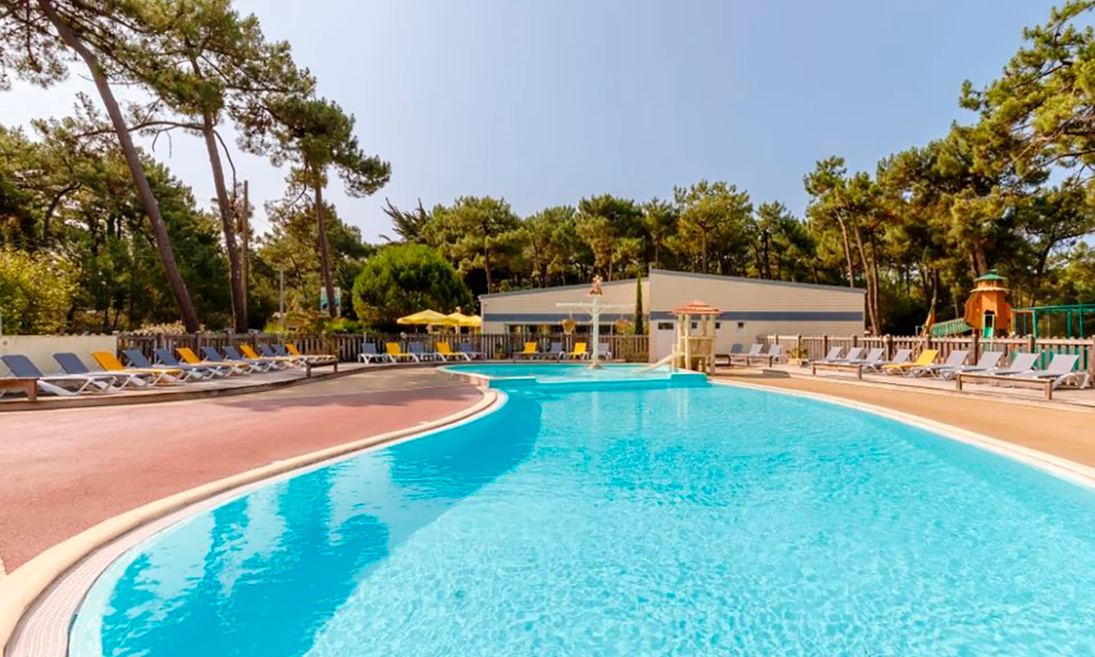 Pool reflecting clear sky with several loungers lined up, surrounded by tall pine trees at Camping 2 Plages & Océan Village Corsaire