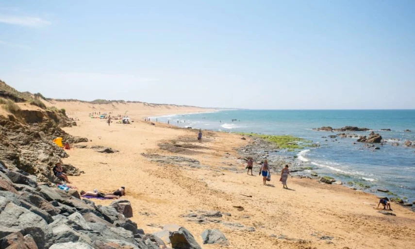 People walking and relaxing on a sandy beach with rocks, beside calm ocean waves at Les Amiaux