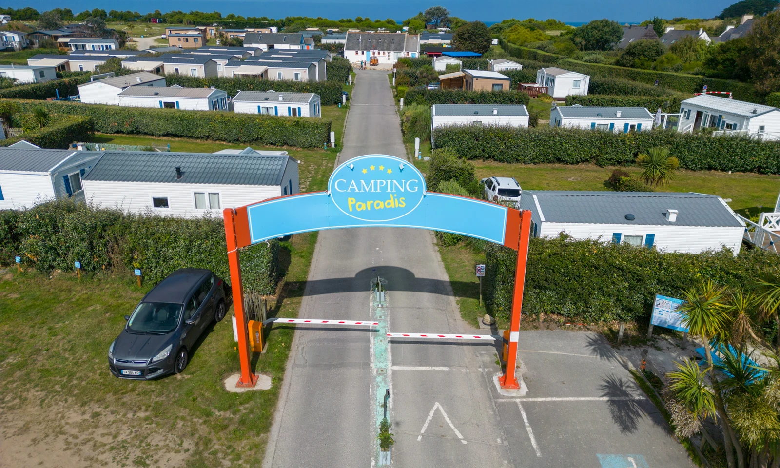 Entrance gate with barrier is positioned prominently; surrounded by neatly arranged mobile homes and green hedges at La Pointe de Roscoff