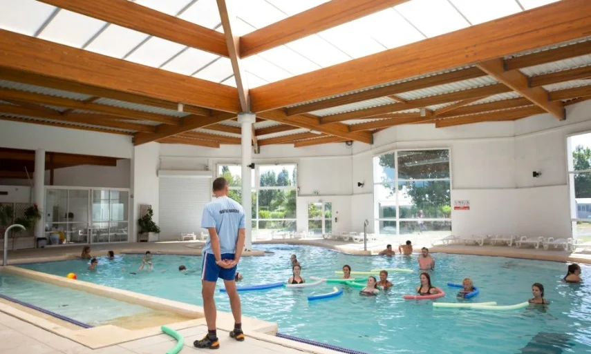 Swim instructor leading a class of adults with pool noodles in an indoor swimming pool at Les Amiaux