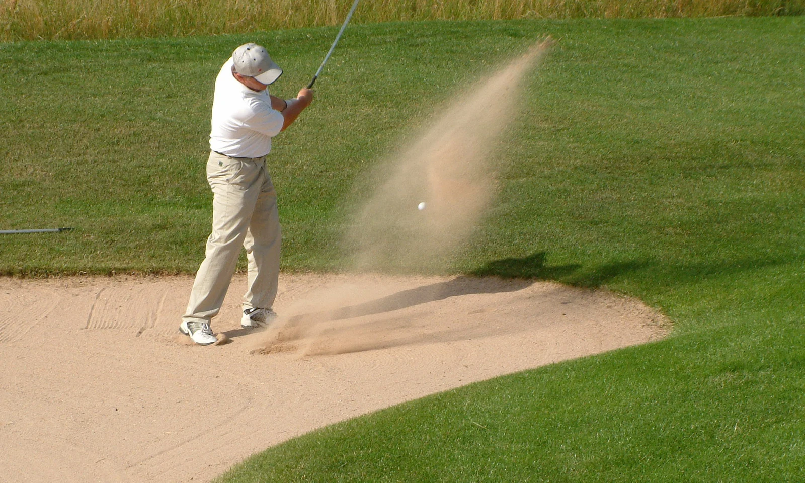 Golfer striking ball from bunker, sand flying, on green golf course at KNAUS Campingpark Hünfeld