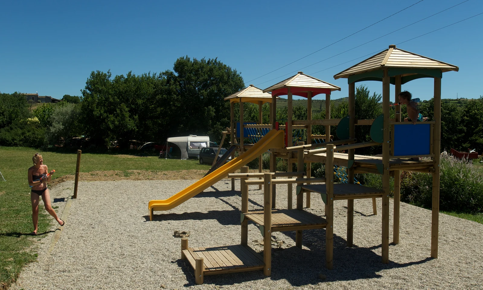 Playground structure with slides and climbing frames, children playing, surrounded by grassy field and trees at Les Arches