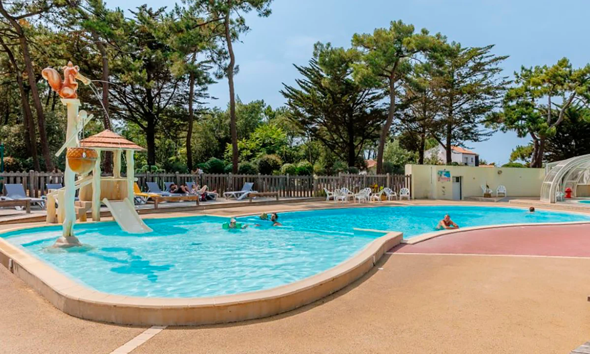 Swimming pool with people relaxing and playing, surrounded by lounge chairs and trees at Camping 2 Plages & Océan Village Corsaire