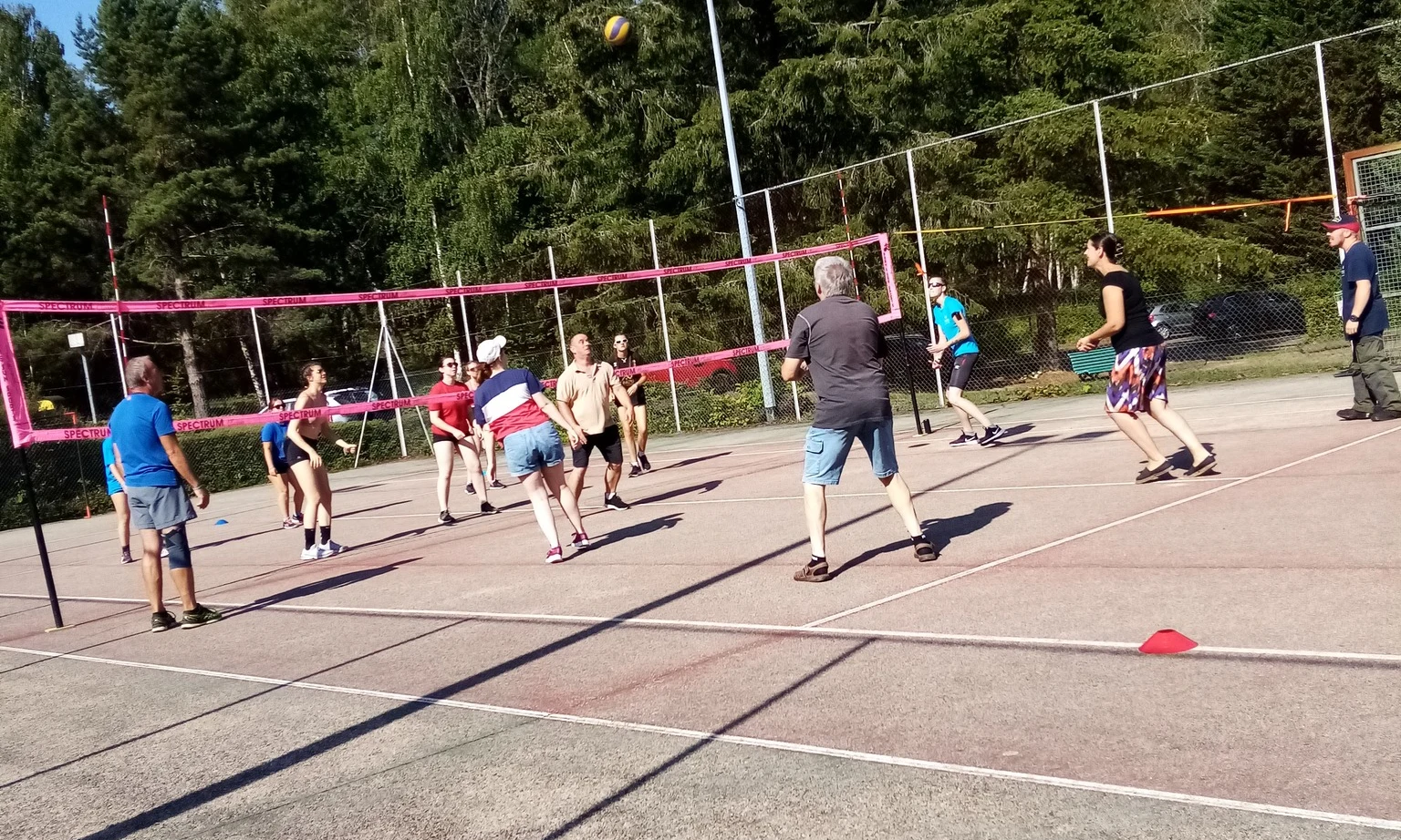 People playing volleyball on an outdoor court surrounded by a forest, under a clear sky at La Foret