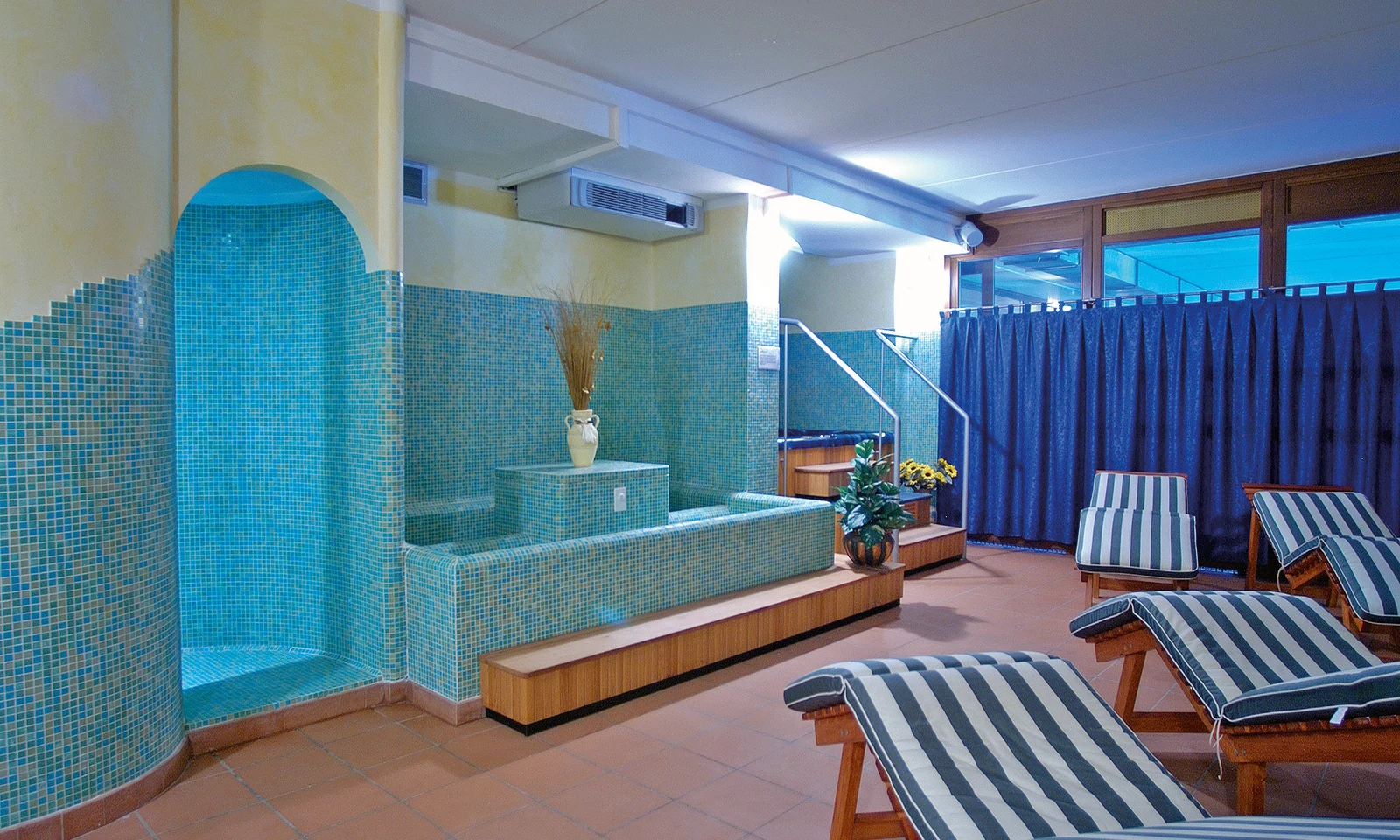 Blue lounge chairs set beside indoor water features, located in a spa area at Residence Campi