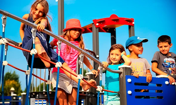 Children climb and play on a colorful playground structure under a blue sky at Les Aventuriers de la Calypso