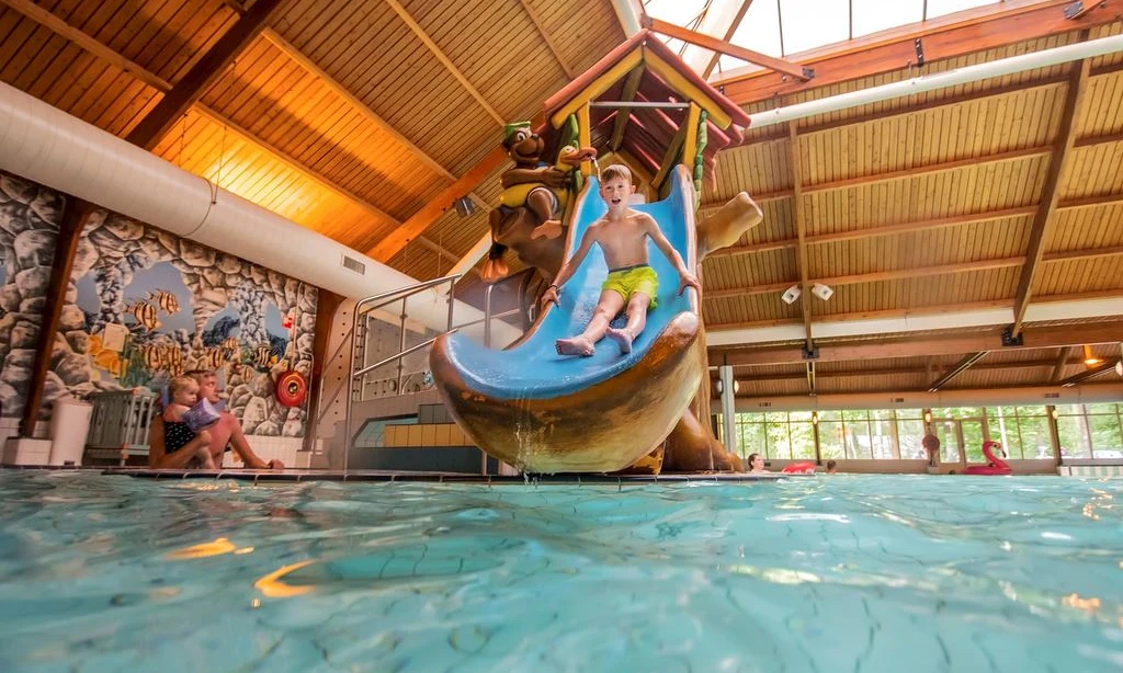 Child sliding down water slide at an indoor pool, surrounded by wooden roof and walls at Landal Rabbit Hill