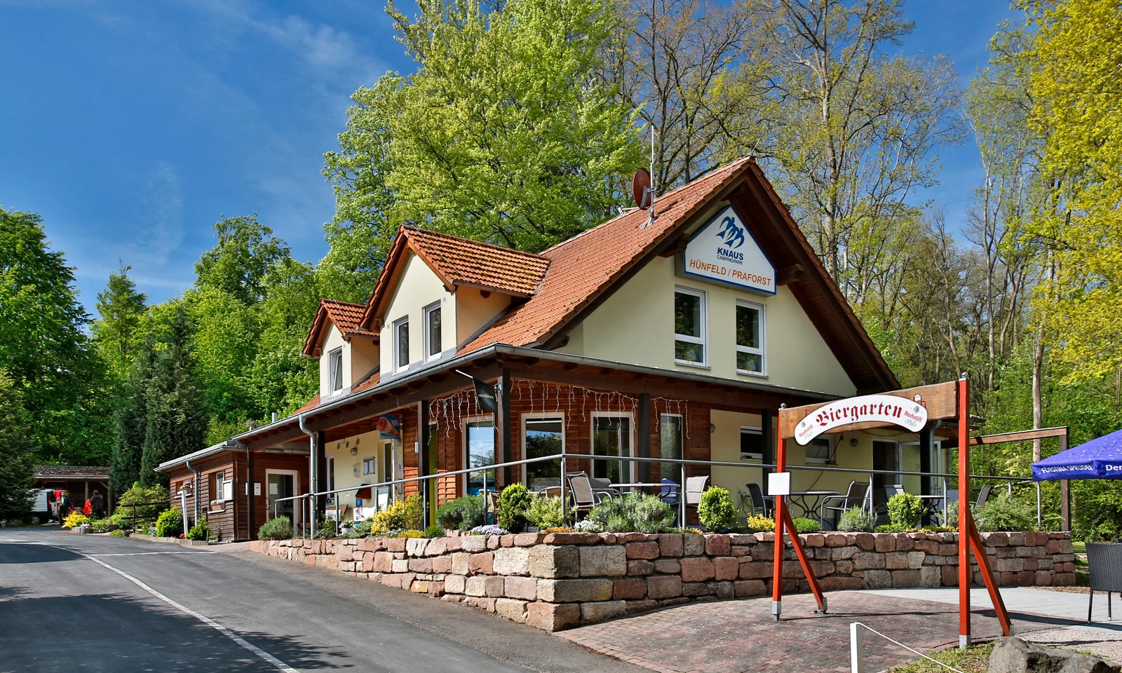 Building with a red-tiled roof, hosting a beer garden, surrounded by lush green trees at KNAUS Campingpark Hünfeld