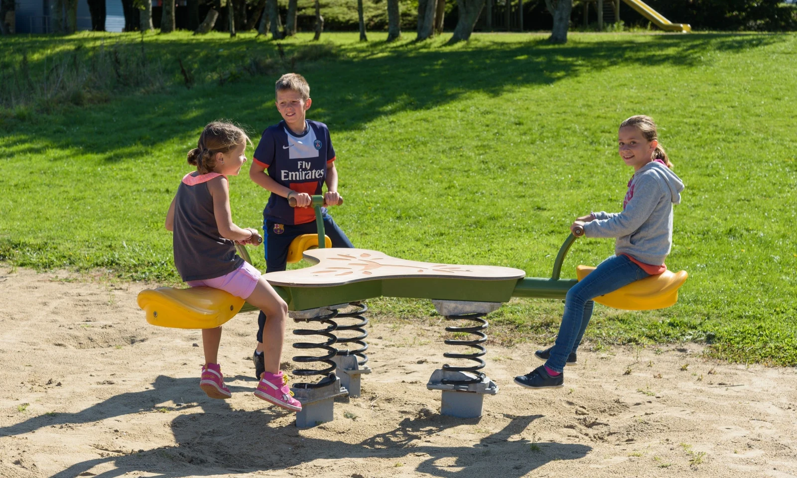 Three children play on a spring-assisted seesaw in a grassy playground area at Domaine de Mesqueau