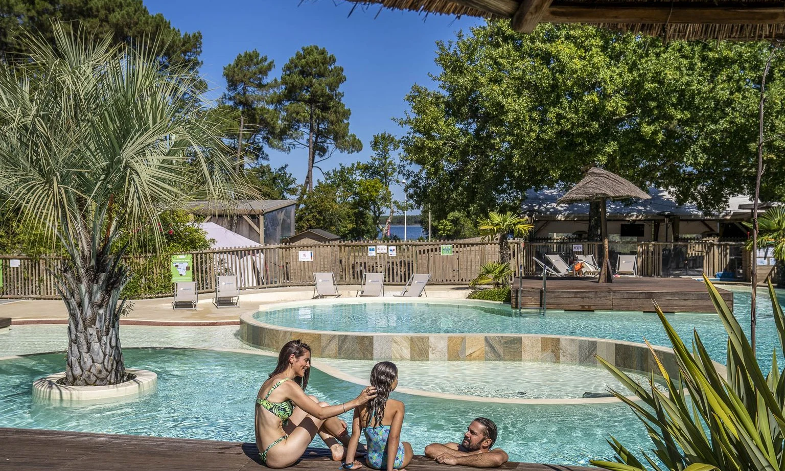 Family relaxing by a pool surrounded by trees and lounge chairs at Lac de Sanguinet