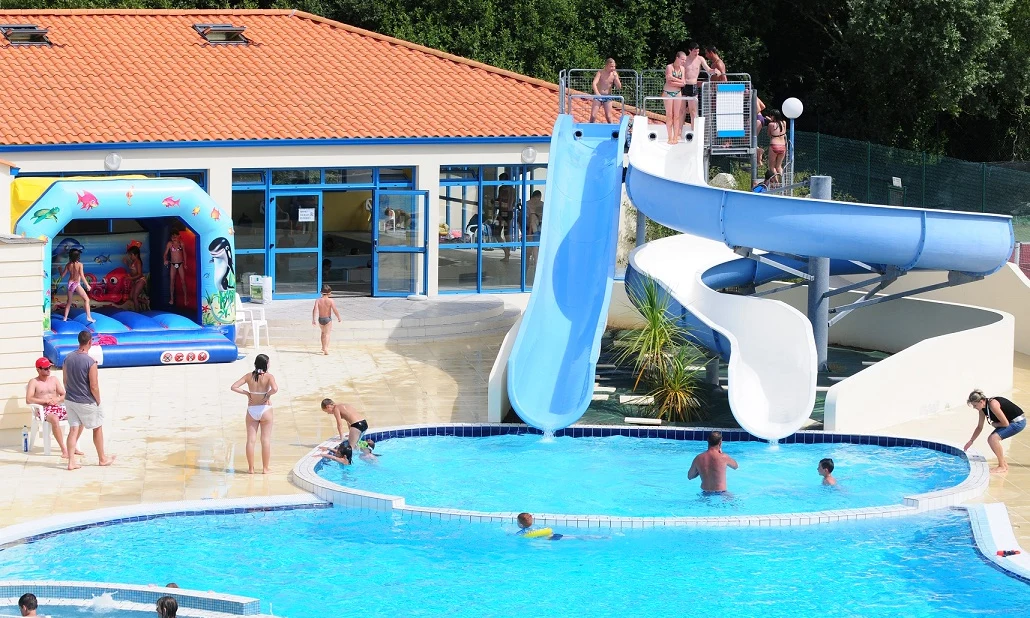 Children playing by the pool and bouncy castle with colorful water slides, beside a red-roofed building at Les Aventuriers de la Calypso