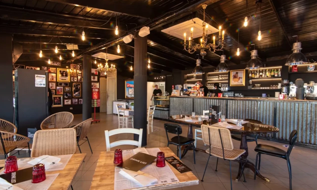 Restaurant interior with rustic tables, chairs, and dim lighting; bar in background with staff at International Riccione Family Camping Village