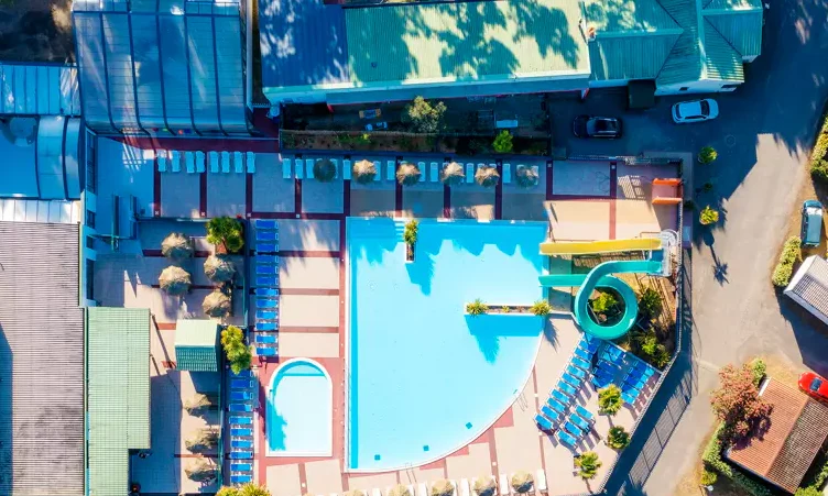 Swimming pool surrounded by lounge chairs and umbrellas, with a winding green waterslide at Le California