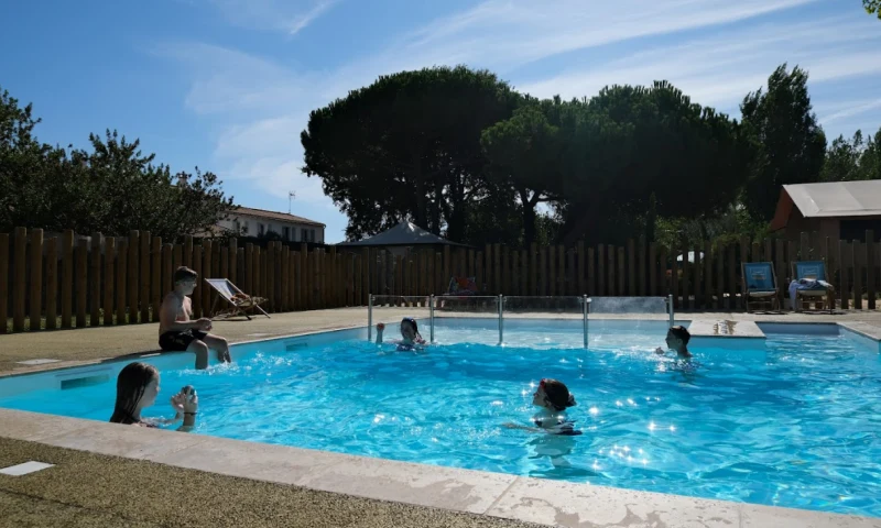 Children swimming and playing in a small outdoor pool surrounded by trees and lounge chairs at Seasonova Ile de Ré