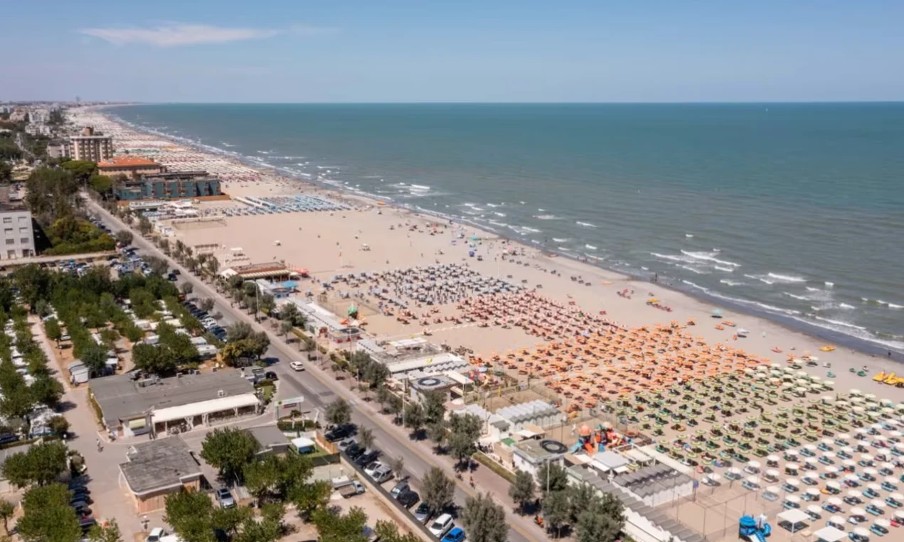 Colorful umbrellas arranged on a sandy beach; people relaxing by the sea in a lively coastal town at International Riccione Family Camping Village