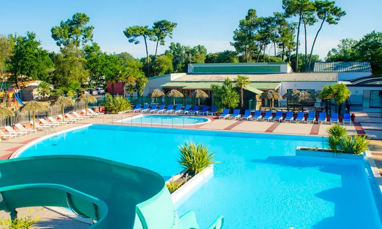 Blue pool with a winding waterslide, surrounded by lounge chairs, parasols, and greenery in a sunny outdoor resort at Le California