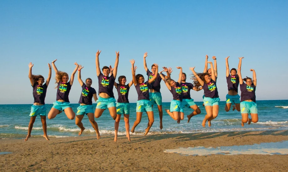 People joyfully jumping on a beach against a blue sky and ocean backdrop at International Riccione Family Camping Village