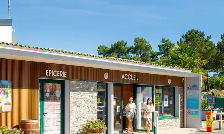 Two women exit a small grocery and reception building with wooden accents and stone walls, surrounded by trees at Le California