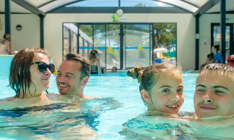 People relaxing and smiling in an indoor pool with a glass roof; others visible outside at Le California