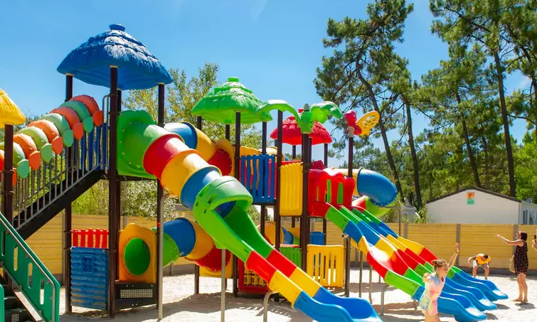 Colorful playground structure with slides and tunnels; children playing energetically; surrounded by trees and clear sky at Le California