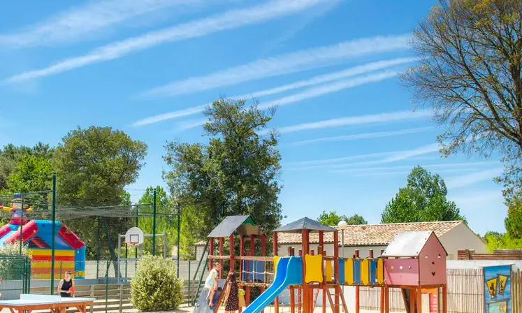 Playground with slides and climbing structures surrounded by trees, picnic tables, and colorful inflatable at Le California