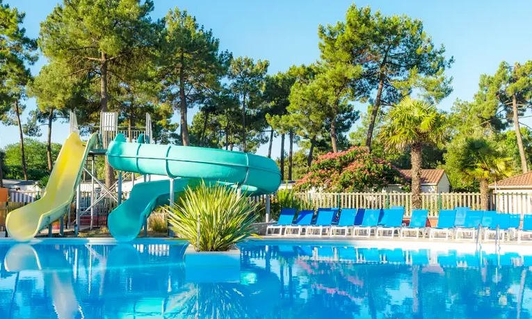 Pool with slides surrounded by lounge chairs amidst trees at Le California