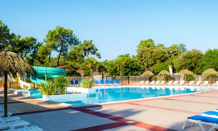 A tranquil swimming pool with slides surrounded by lounge chairs and tall trees at Le California