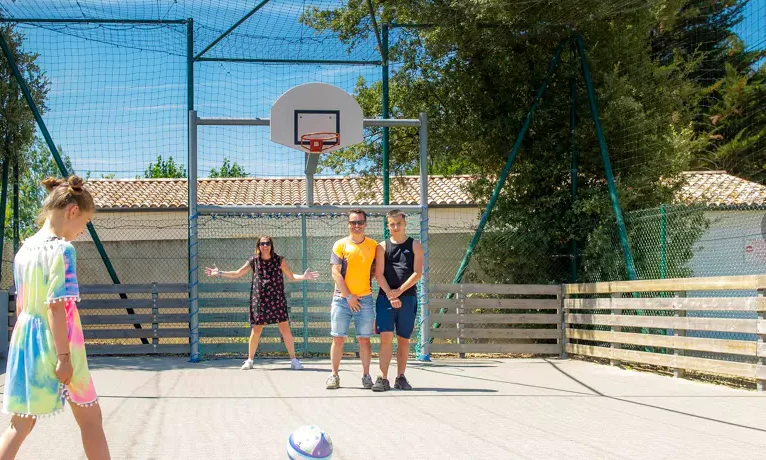 People playing on a fenced basketball court outdoors near trees and a building at Le California