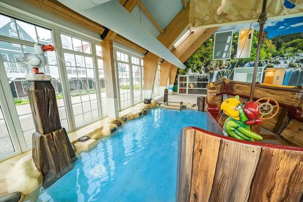 Kid's indoor pool with playful pirate ship and seagull sculpture, surrounded by large windows and nature-themed murals at Europarcs Poort van Amsterdam