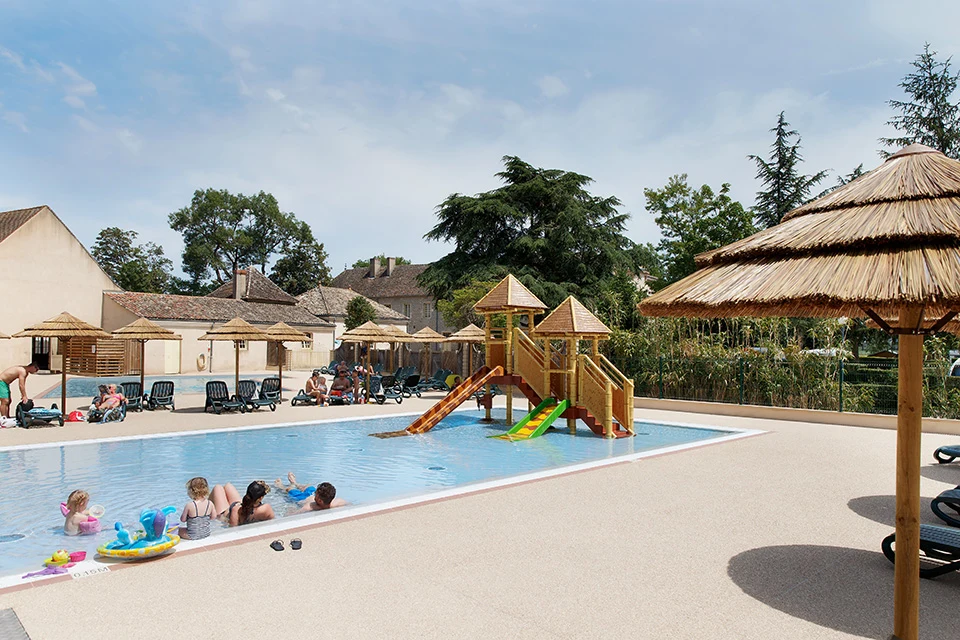 Children's pool with water slides and lounge chairs surrounded by straw parasols and buildings at Château de l'Epervière
