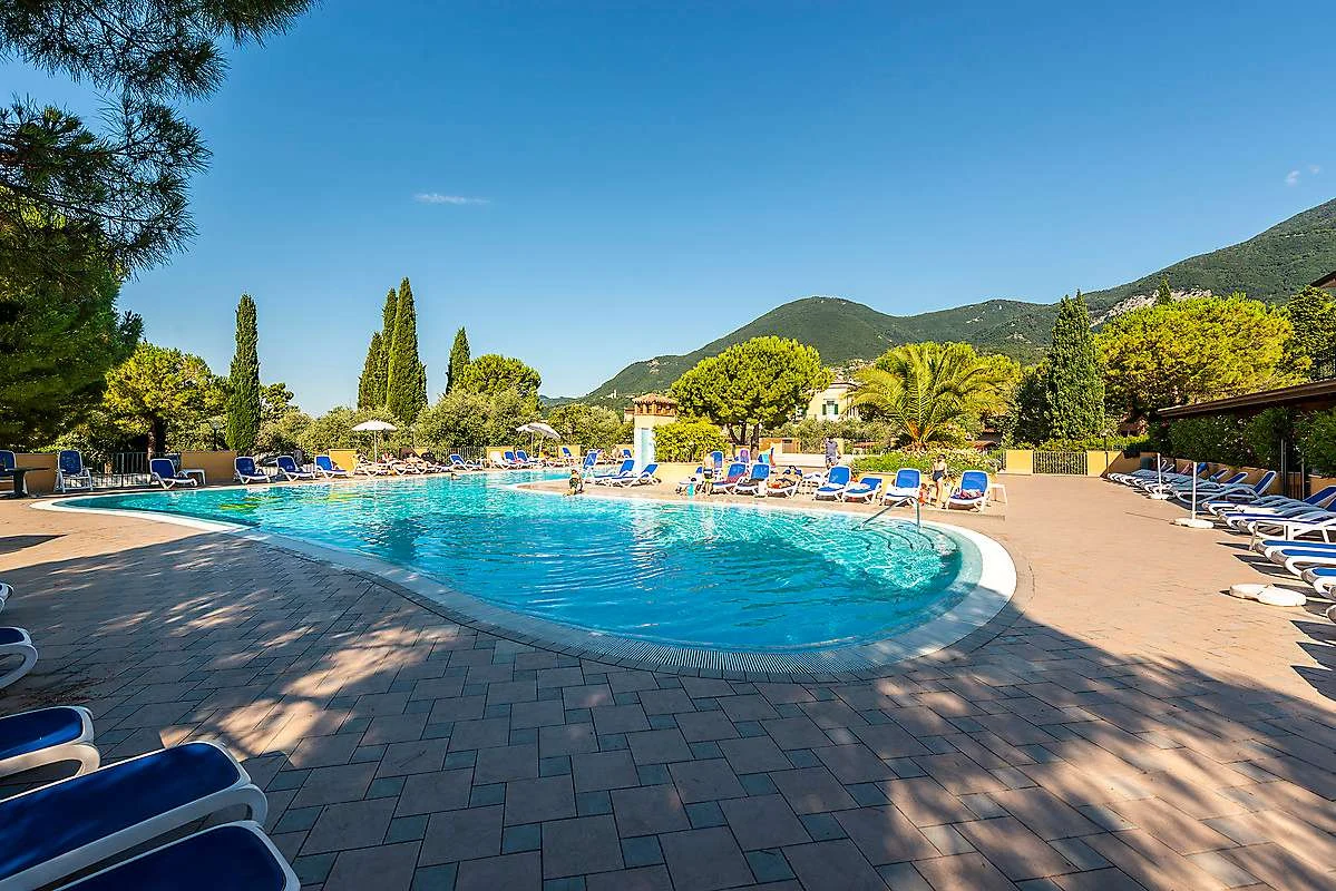 Outdoor swimming pool with sun loungers surrounded by trees and mountains at Toscolano