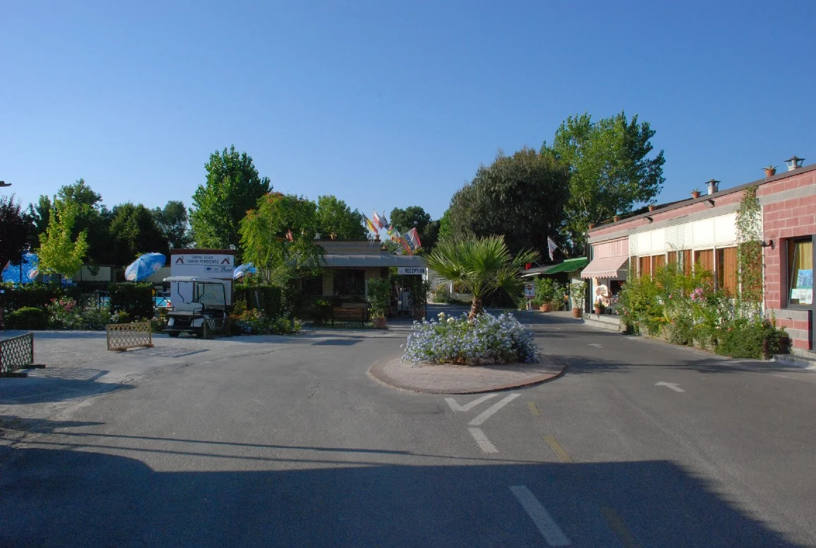Golf cart parked near flowerbeds and buildings under a clear sky, surrounded by trees at Village Torre Pendente