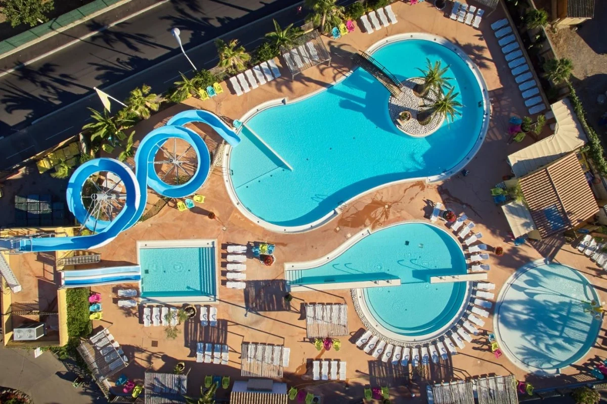 Aerial view of multiple swimming pools with blue water slides, surrounded by sun loungers and palm trees at Les Mediterranées Nouvelle Floride