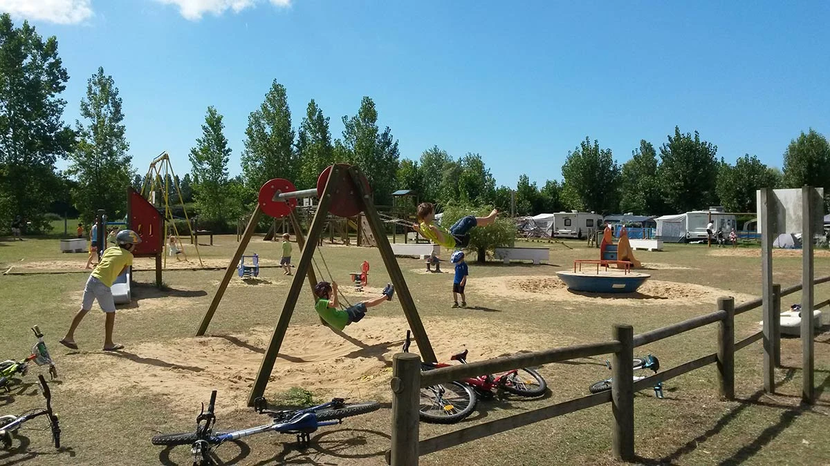 Children swinging and playing in a playground surrounded by trees and campers at La Yole 