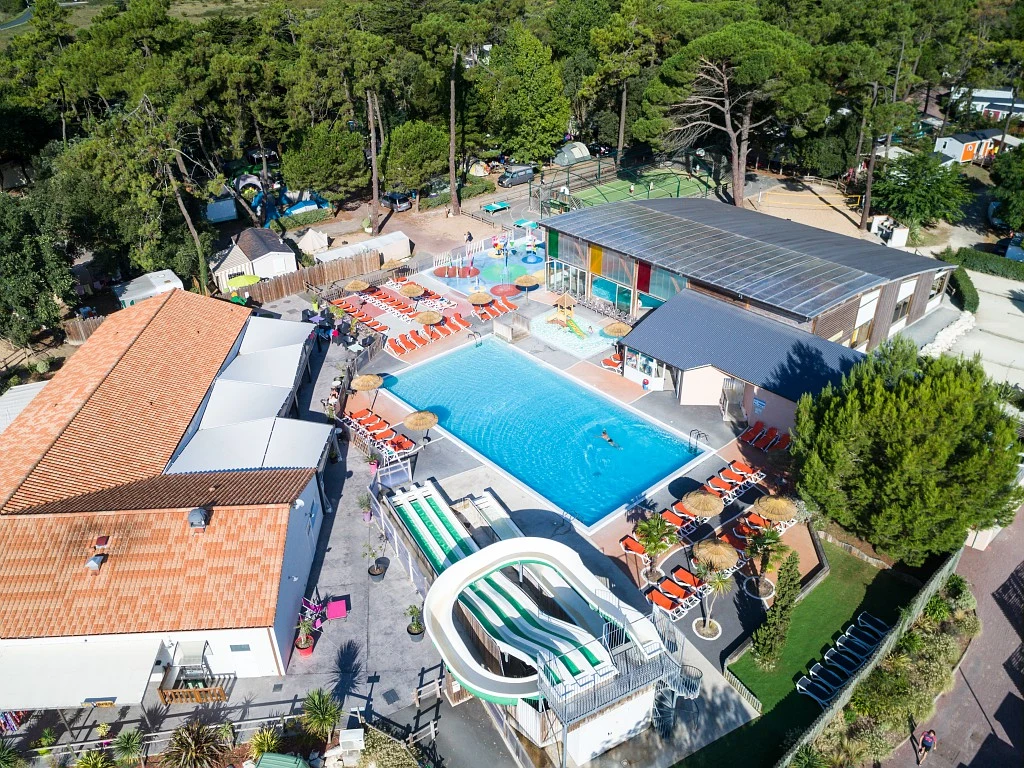 Swimming pool with a waterslide surrounded by loungers and buildings, nestled in a forested campsite at Signol