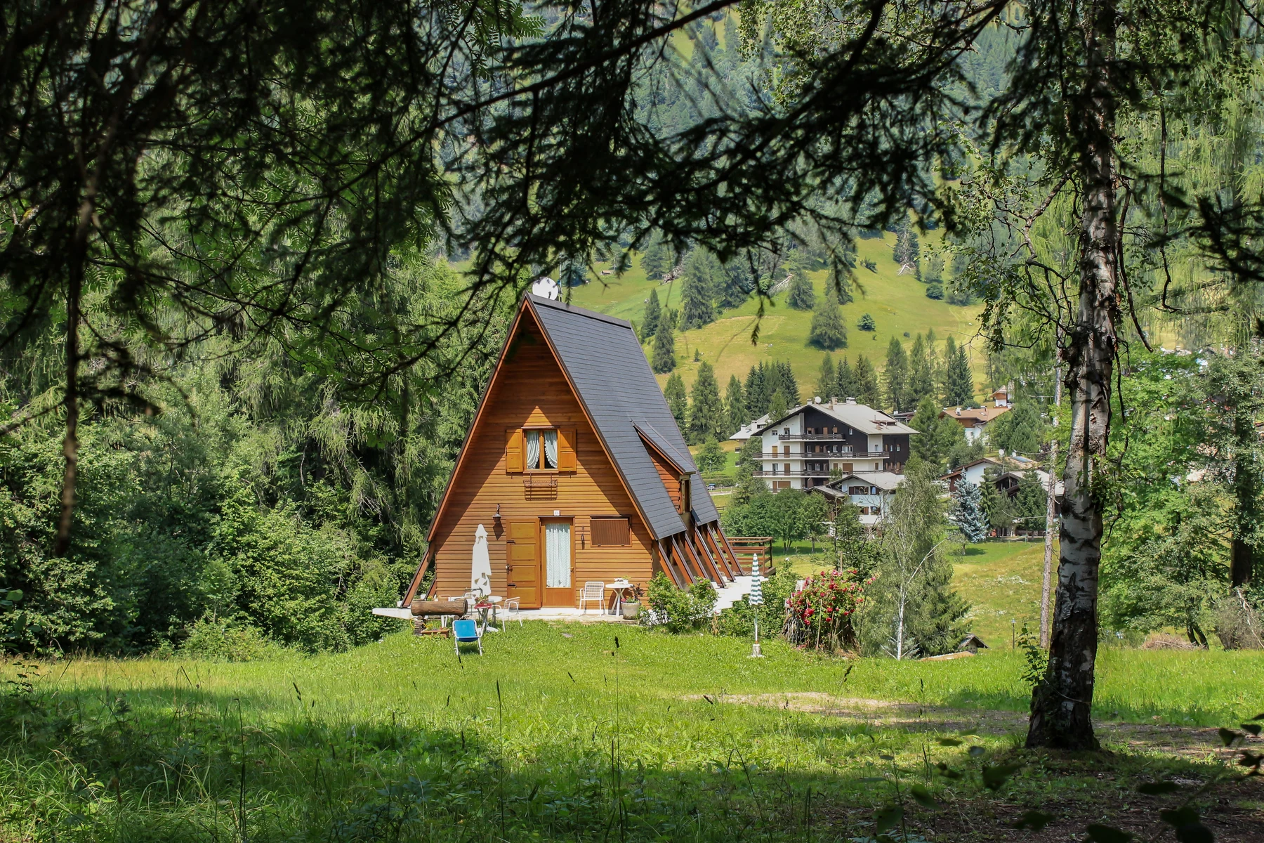 A-frame cabin surrounded by lush greenery and distant houses at Fiemme Village