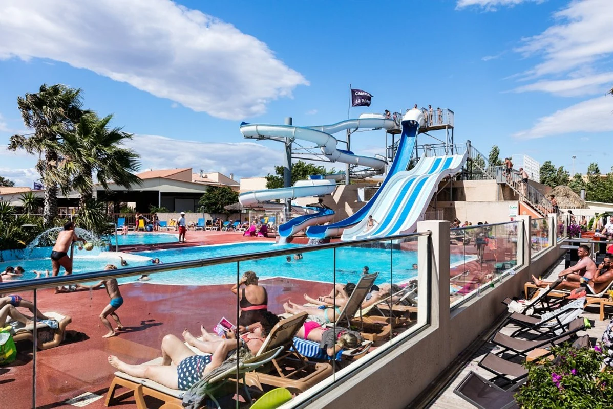 People relaxing and playing around a large pool with slides and loungers under a clear sky at La Plage et le Bord de mer