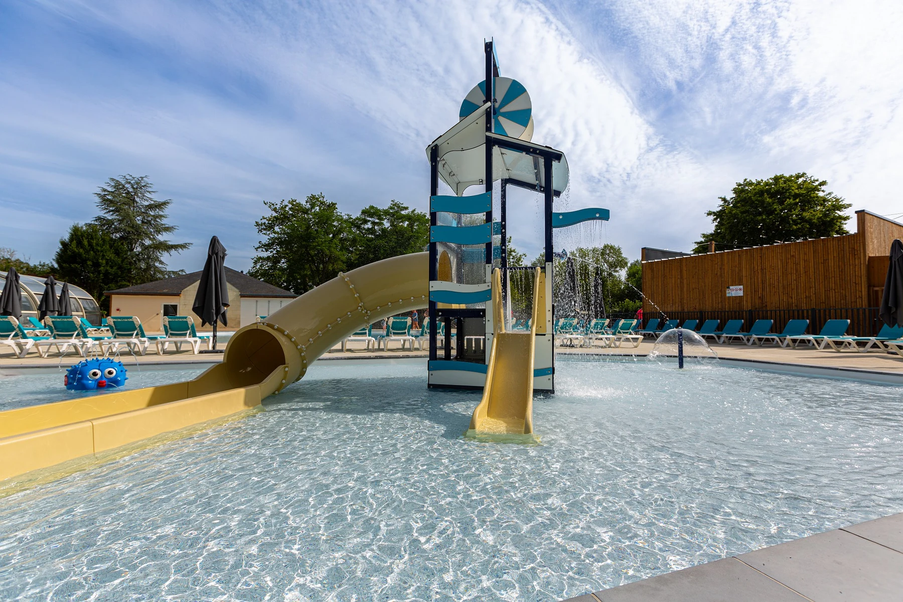 Children’s water play area with slides and sprinklers, surrounded by lounge chairs under a partly cloudy sky at Marvilla Parks Le Domaine de la Brèche