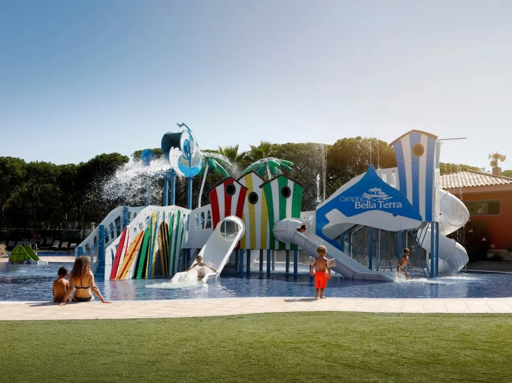 Children playing on colorful water slides and structures in a pool area surrounded by trees at Bella Terra