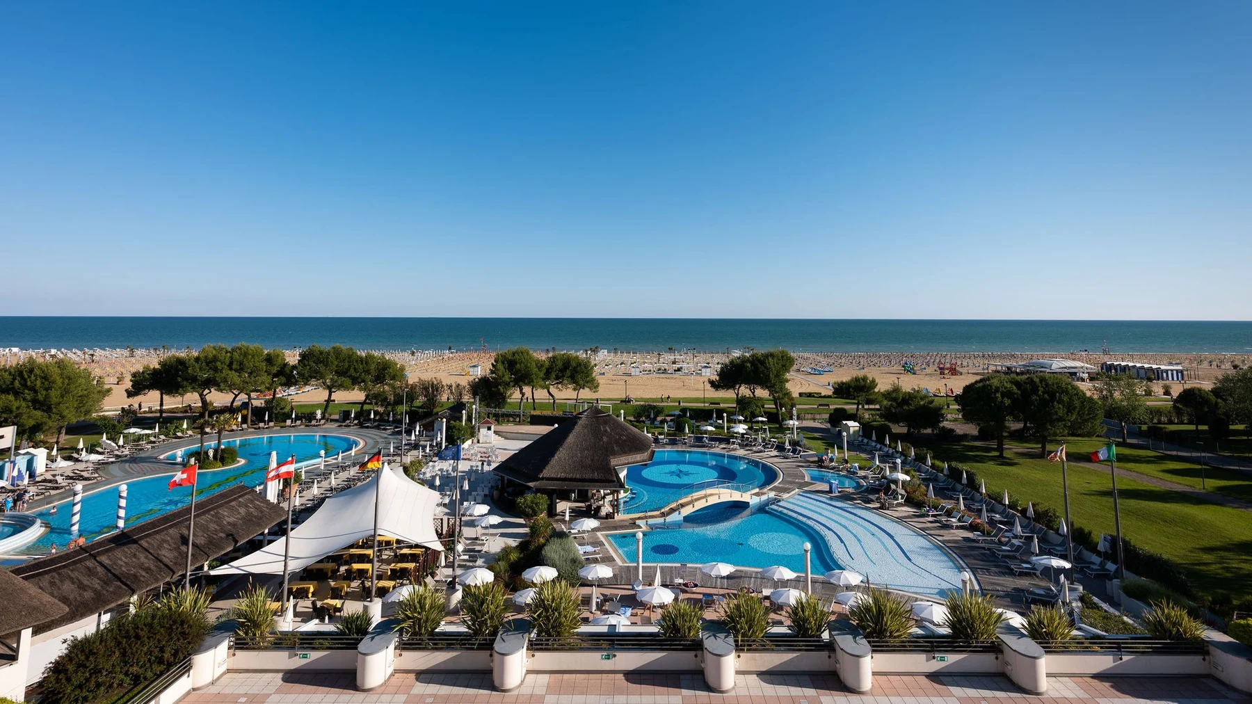 Beachside resort features pools and trees near a sandy shore with calm sea and clear sky at Savoy Beach Hotel & Thermal Spa