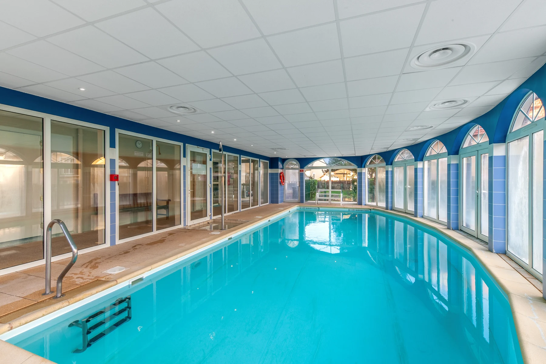 Indoor swimming pool surrounded by glass doors and windows, with blue walls and white ceiling at Port Guillaume