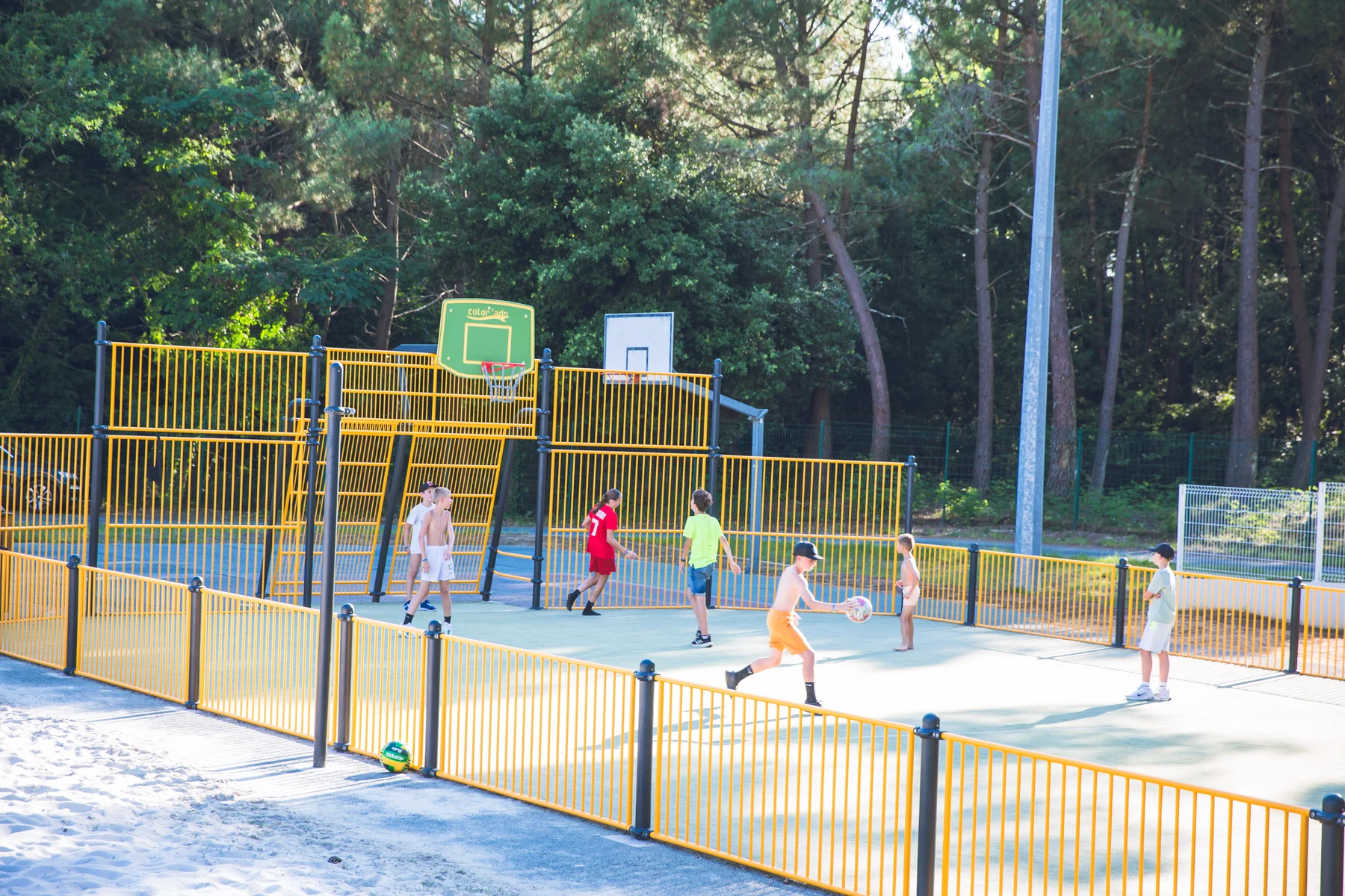 Children playing basketball on a fenced court, surrounded by tall trees at Domaine de Montcalm