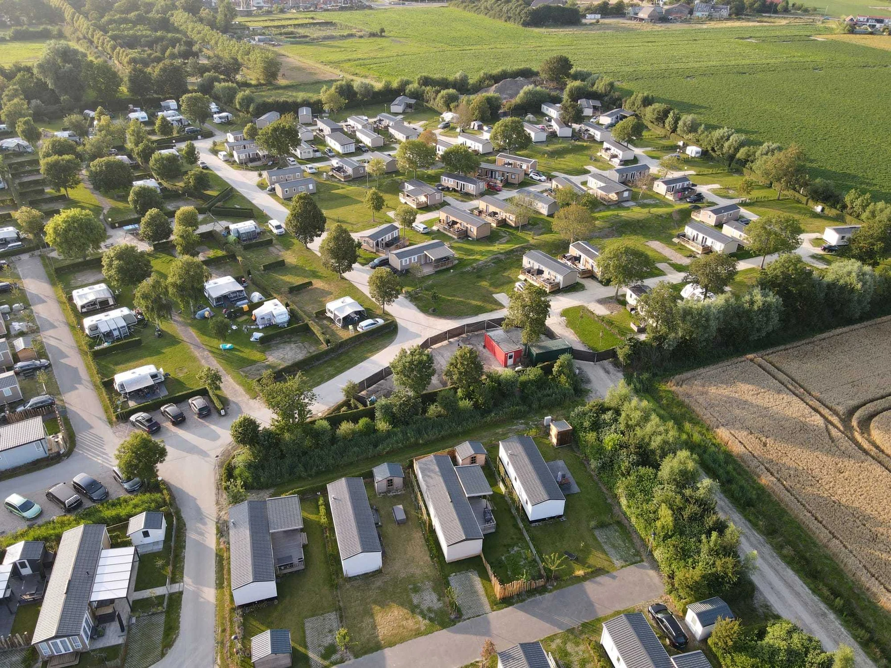 Aerial view of numerous cabins and tents situated on green plots surrounded by trees and roads, with fields nearby at In de Bongerd