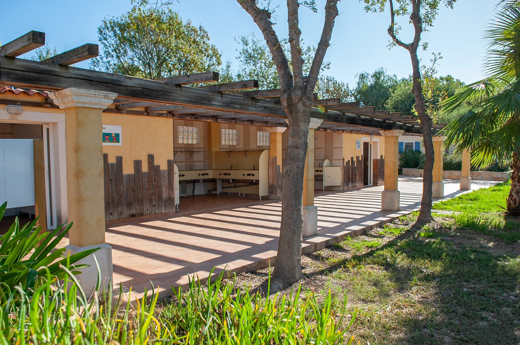 Outdoor wash area and restrooms with sinks under a wooden pergola, surrounded by trees and greenery at Port Pothuau