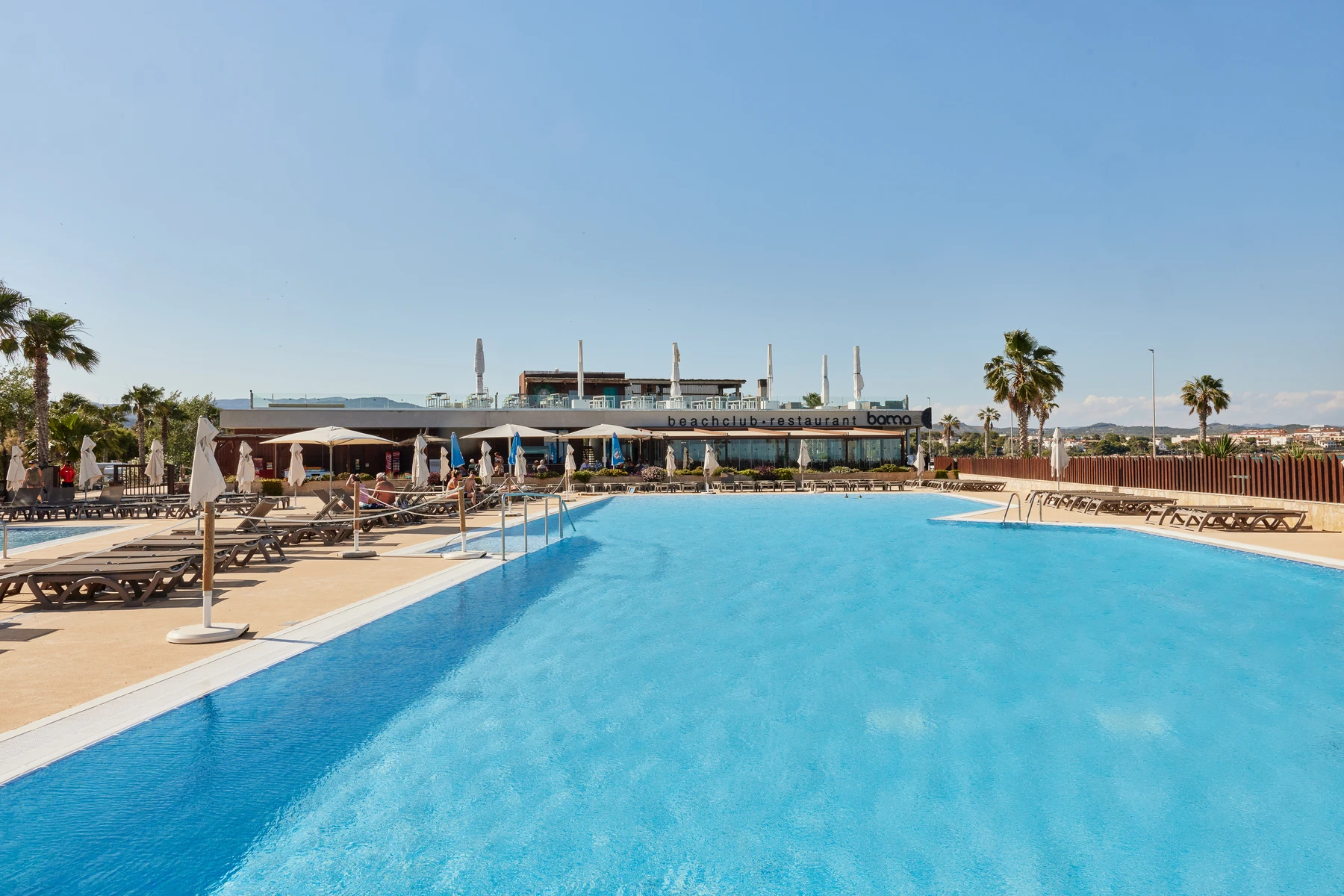 A clear blue swimming pool, surrounded by sun loungers and umbrellas, is located near a beachside restaurant at Taïga Delta De L'Ebre