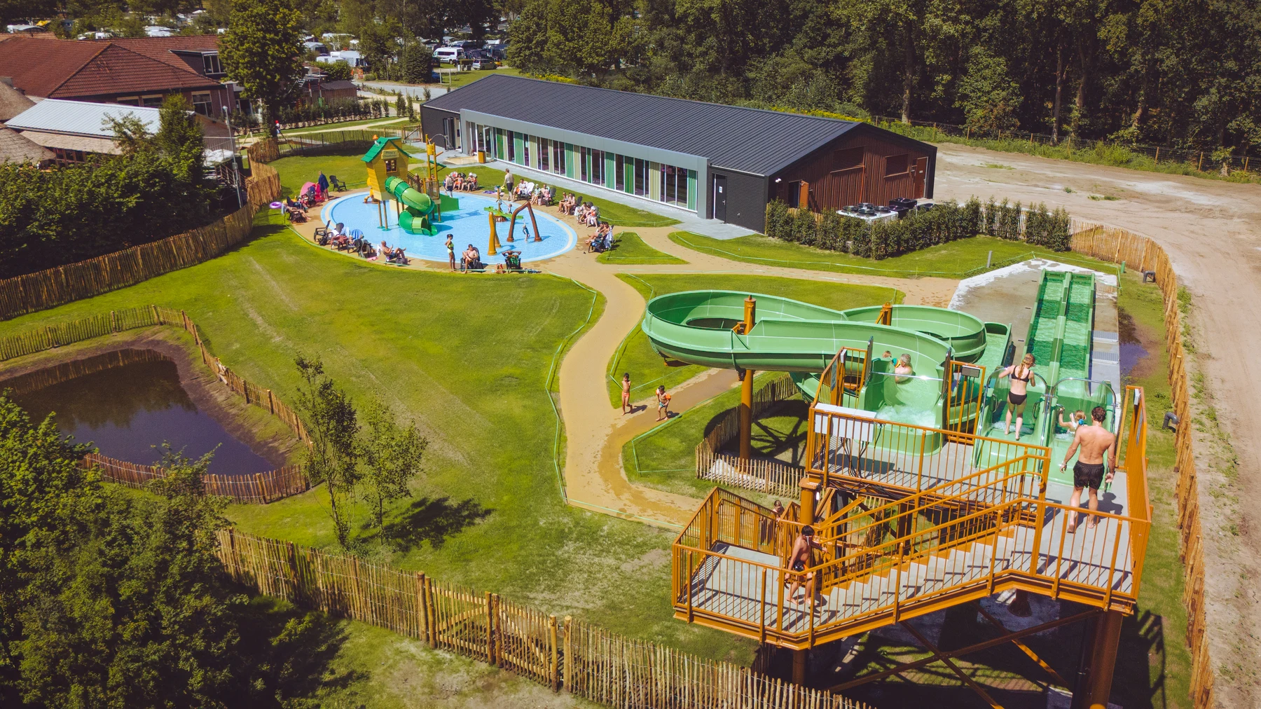 Children enjoy green water slides in a vibrant outdoor pool area, surrounded by grass and trees at Marvilla Parks Kaatsheuvel