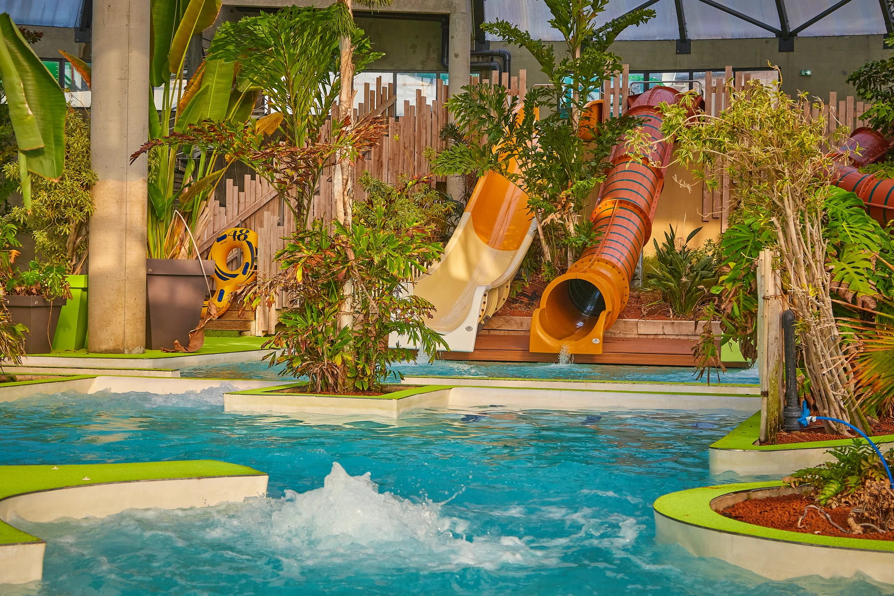 Waterslides empty water into a turquoise pool surrounded by lush tropical plants and green areas at Le Domaine d'Inly