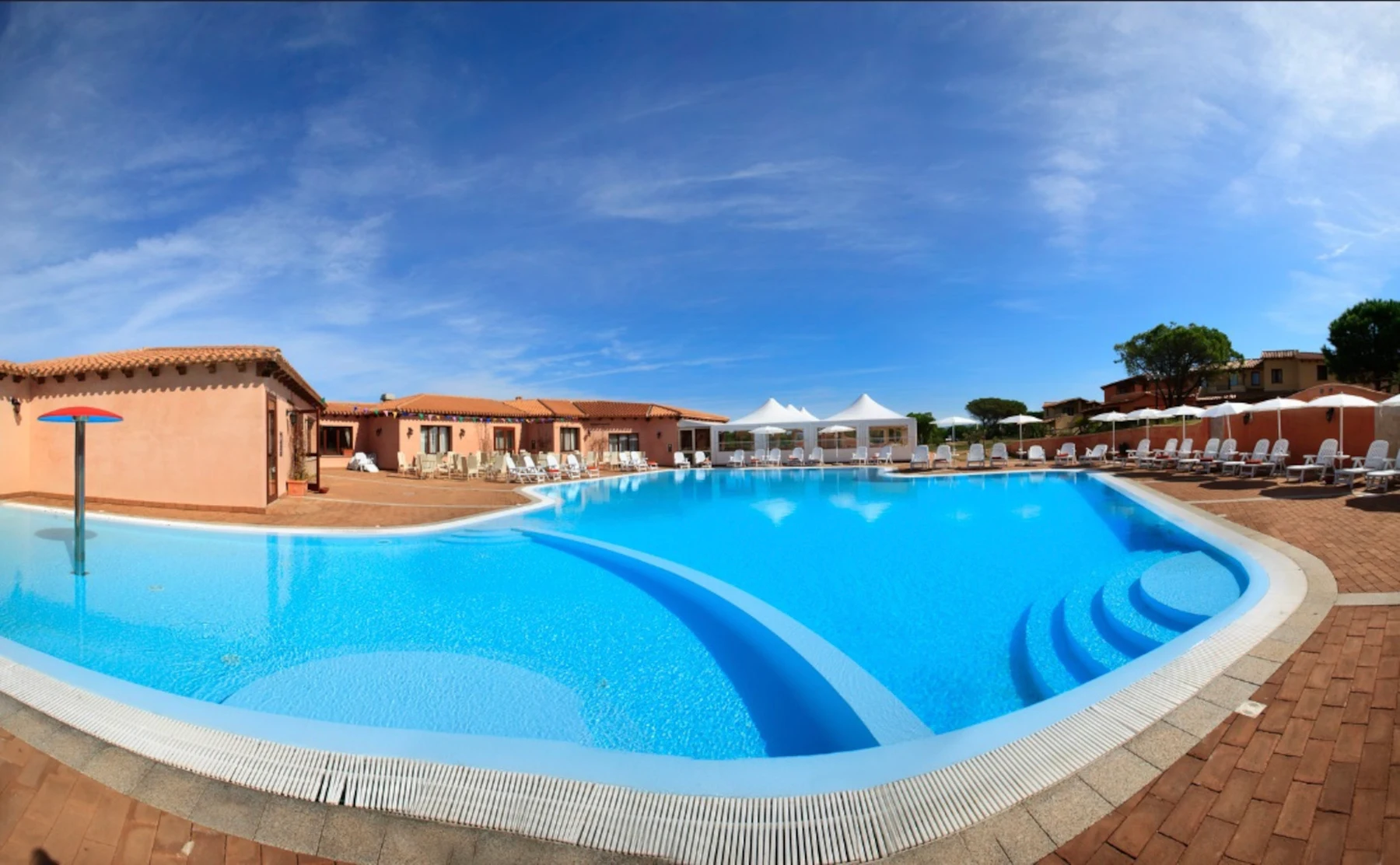 A large swimming pool with sun loungers on a tiled deck, adjacent to a building complex under a clear blue sky at Residence Vignola Mare