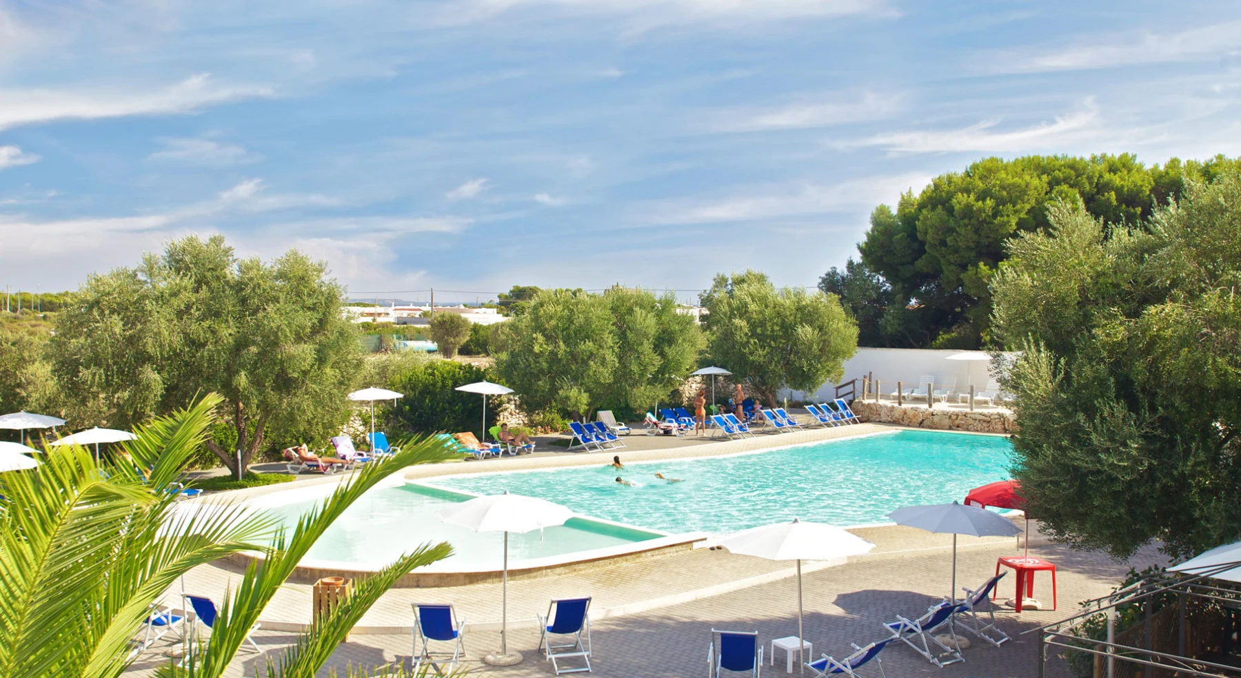Swimming pool surrounded by lounge chairs and trees under a clear sky at Porto Cesareo Camping